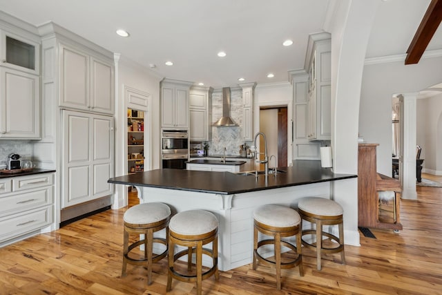 kitchen with wall chimney exhaust hood, sink, ornate columns, a kitchen breakfast bar, and white cabinets