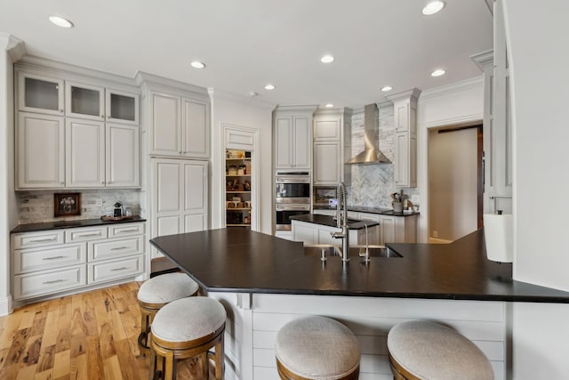 kitchen with sink, crown molding, white cabinetry, a kitchen bar, and wall chimney exhaust hood