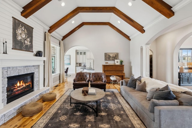 living room with hardwood / wood-style flooring, a stone fireplace, high vaulted ceiling, and beam ceiling