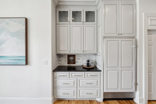 bar with tasteful backsplash, white cabinets, and light wood-type flooring