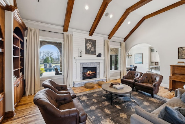 living room with a fireplace, light wood-type flooring, and vaulted ceiling with beams