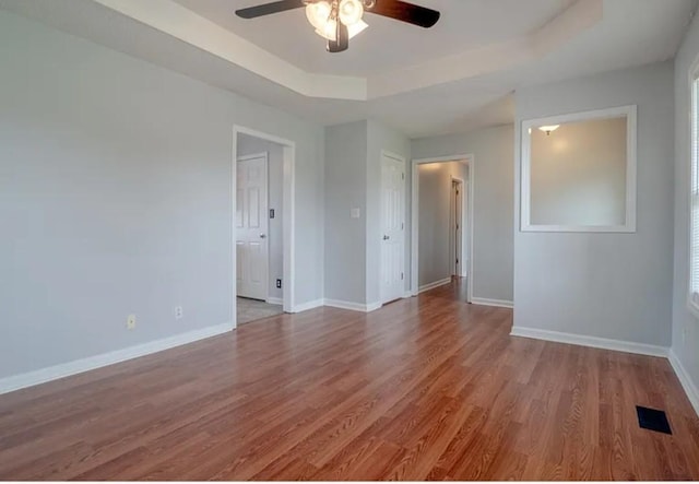 unfurnished room with a raised ceiling, ceiling fan, and light hardwood / wood-style floors