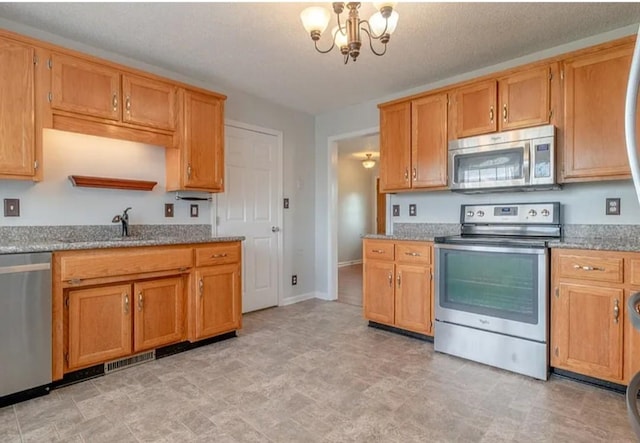 kitchen with light stone counters, stainless steel appliances, sink, and a notable chandelier