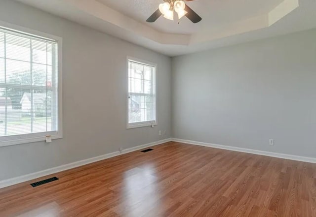 unfurnished room with ceiling fan, plenty of natural light, a raised ceiling, and wood-type flooring