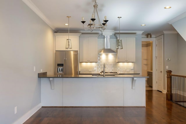 kitchen featuring decorative light fixtures, white cabinets, kitchen peninsula, high end fridge, and wall chimney exhaust hood