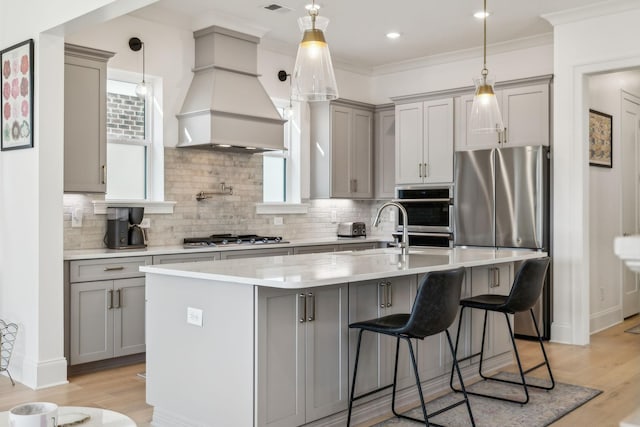 kitchen featuring premium range hood, sink, gray cabinetry, appliances with stainless steel finishes, and a kitchen island with sink