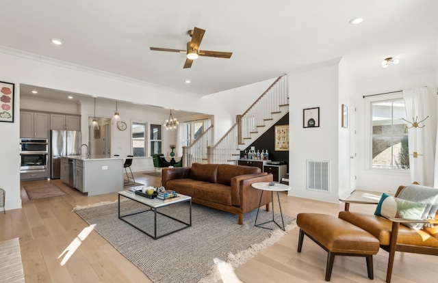 living room with ornamental molding, sink, ceiling fan with notable chandelier, and light wood-type flooring