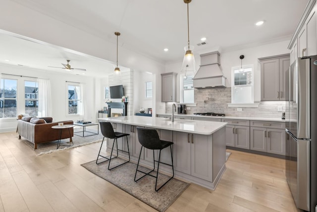 kitchen with appliances with stainless steel finishes, pendant lighting, an island with sink, sink, and custom range hood