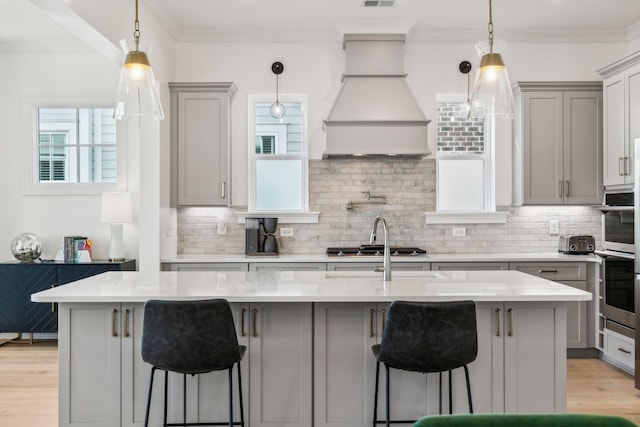 kitchen featuring a breakfast bar, custom exhaust hood, a center island with sink, and gray cabinetry