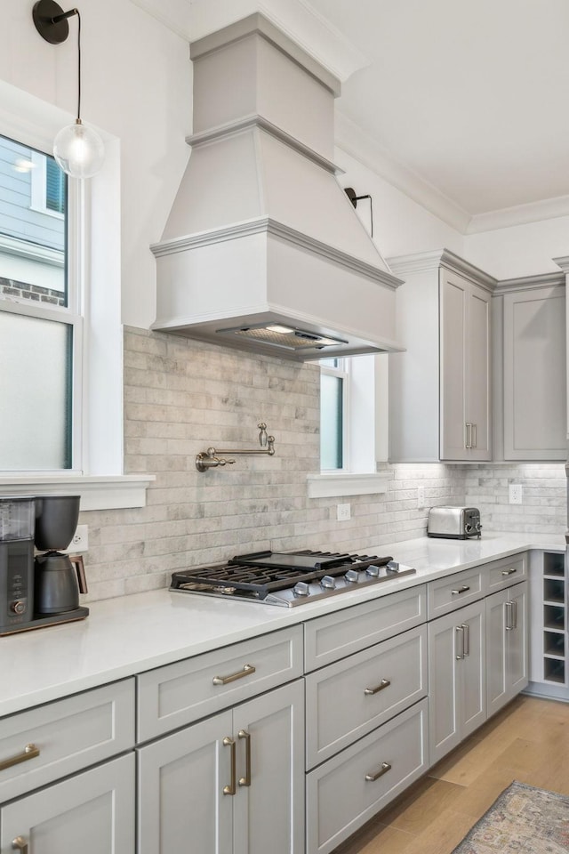 kitchen featuring premium range hood, pendant lighting, stainless steel gas stovetop, backsplash, and ornamental molding