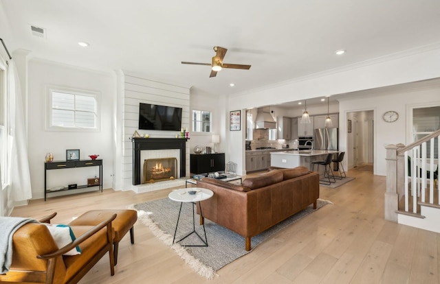 living room with ornamental molding, ceiling fan, a fireplace, and light hardwood / wood-style floors