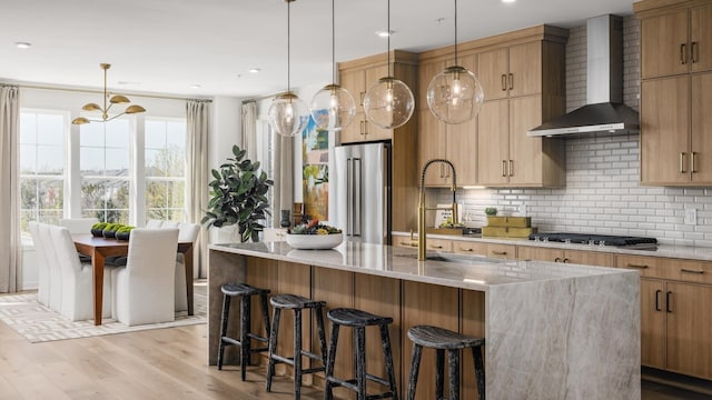 kitchen featuring light stone countertops, decorative light fixtures, stainless steel appliances, and wall chimney exhaust hood