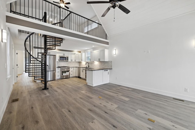 unfurnished living room featuring ceiling fan, high vaulted ceiling, sink, and light wood-type flooring