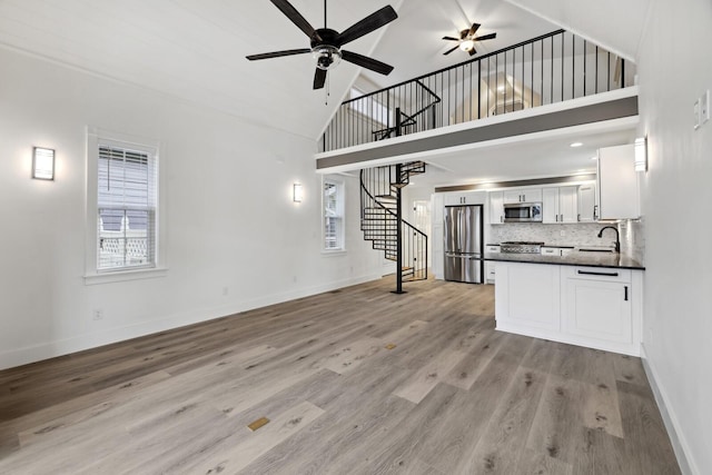 unfurnished living room with ceiling fan, high vaulted ceiling, sink, and light hardwood / wood-style floors