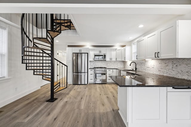 kitchen featuring dark stone countertops, stainless steel appliances, light hardwood / wood-style floors, white cabinets, and kitchen peninsula