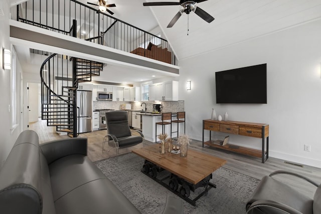 living room featuring ceiling fan, high vaulted ceiling, sink, and light hardwood / wood-style floors