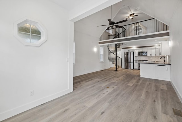 unfurnished living room featuring ceiling fan, high vaulted ceiling, sink, and light hardwood / wood-style floors