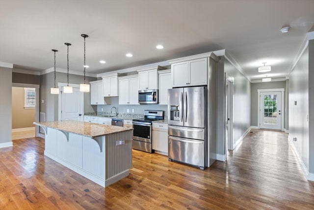 kitchen featuring appliances with stainless steel finishes, white cabinetry, a kitchen bar, a center island, and light stone countertops