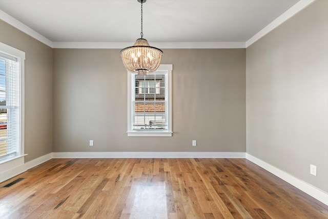 empty room with a wealth of natural light, hardwood / wood-style floors, and a chandelier