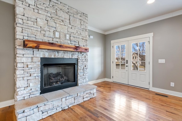 unfurnished living room with hardwood / wood-style flooring, crown molding, a stone fireplace, and french doors