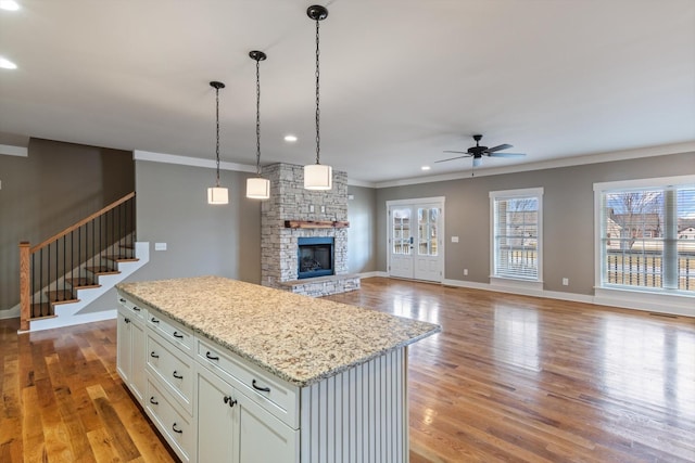 kitchen featuring a stone fireplace, a center island, white cabinets, and light hardwood / wood-style floors