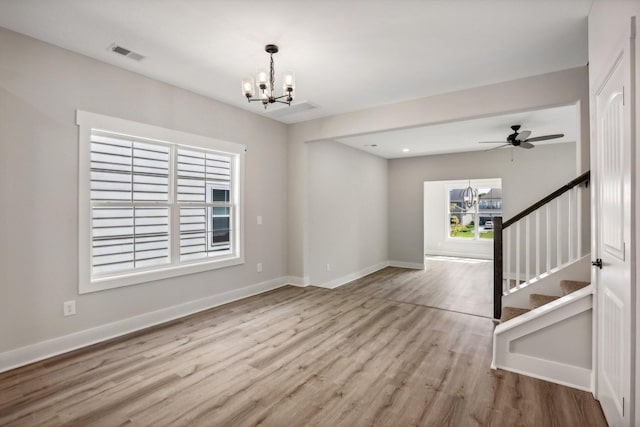 empty room with ceiling fan with notable chandelier and light wood-type flooring