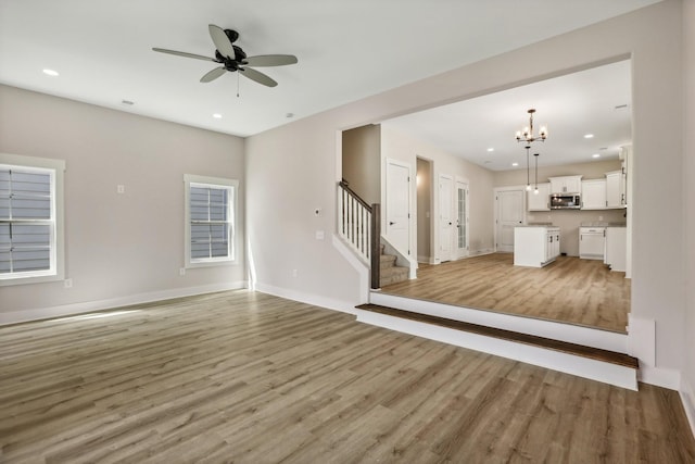 unfurnished living room featuring ceiling fan with notable chandelier and light hardwood / wood-style flooring