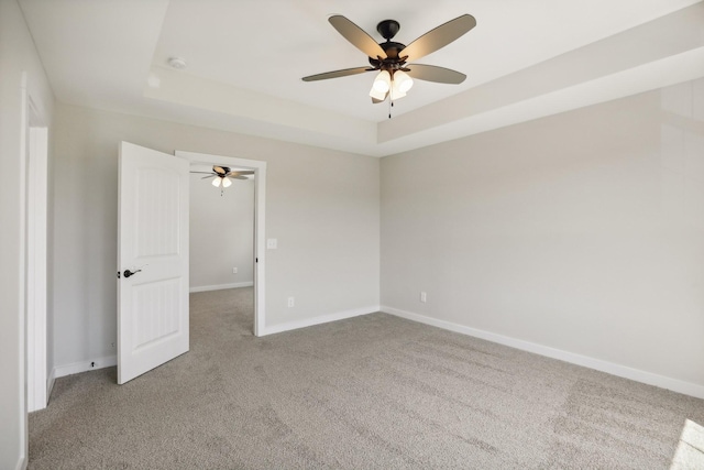 carpeted spare room with a raised ceiling and ceiling fan