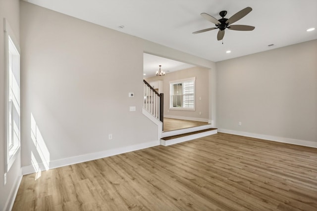 unfurnished room with ceiling fan with notable chandelier and light hardwood / wood-style floors