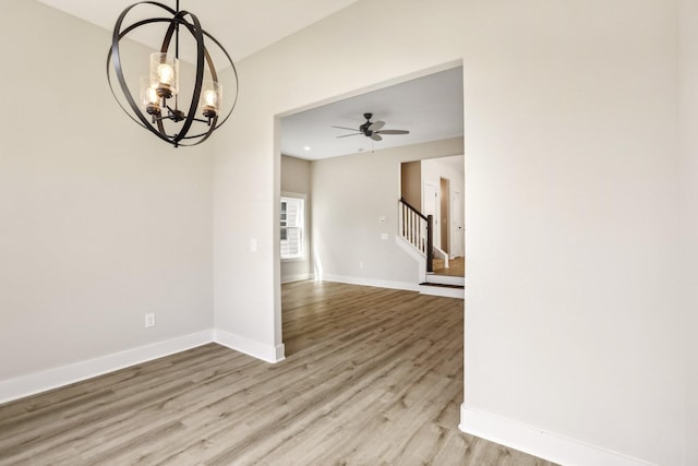 spare room with ceiling fan with notable chandelier and light hardwood / wood-style floors