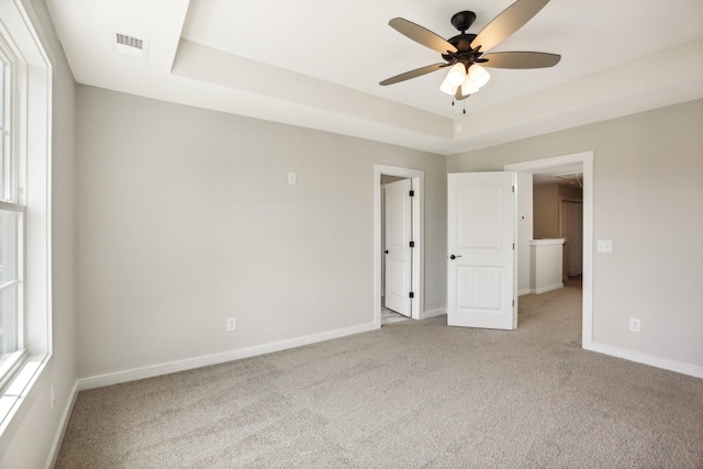 carpeted empty room featuring a healthy amount of sunlight, ceiling fan, and a tray ceiling