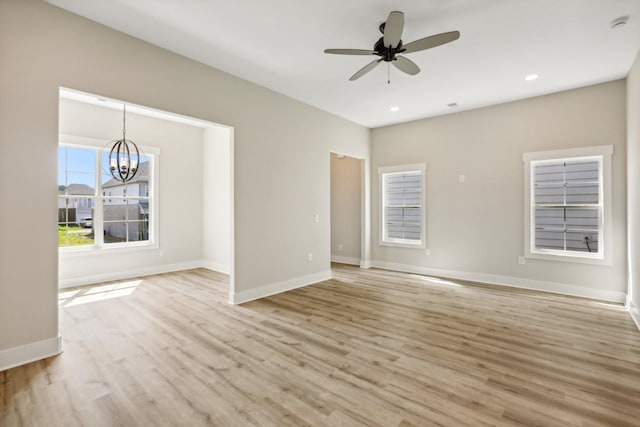 empty room featuring ceiling fan with notable chandelier and light hardwood / wood-style floors