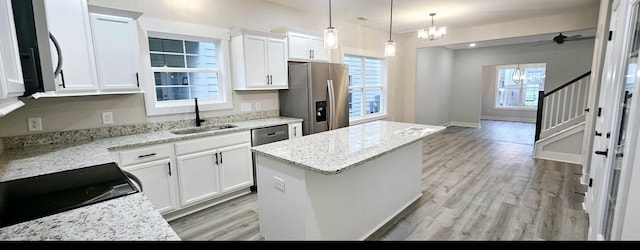 kitchen with white cabinetry, stainless steel appliances, a center island, and light stone countertops