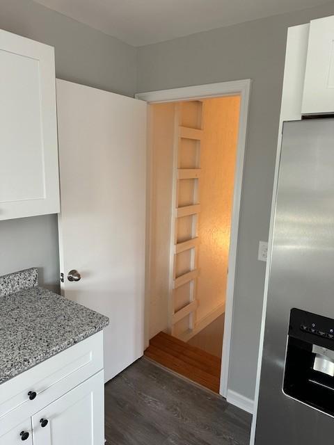 kitchen featuring stainless steel fridge, light stone countertops, dark hardwood / wood-style floors, and white cabinets