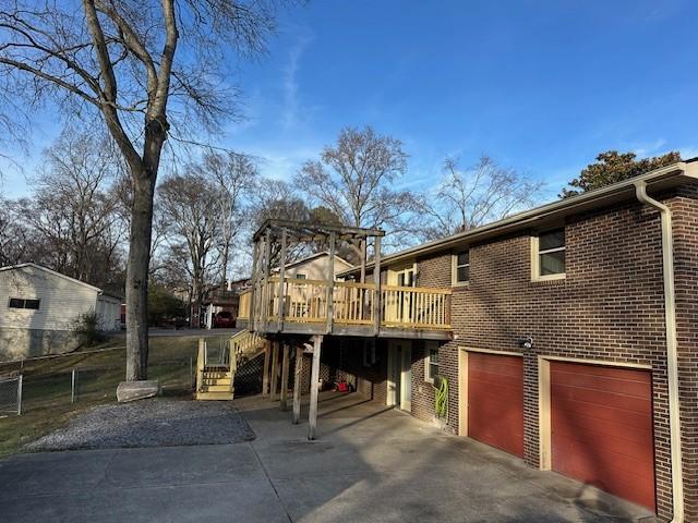 back of house featuring a deck, a garage, brick siding, concrete driveway, and stairway