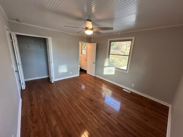 unfurnished bedroom featuring crown molding, ceiling fan, dark hardwood / wood-style floors, and a closet