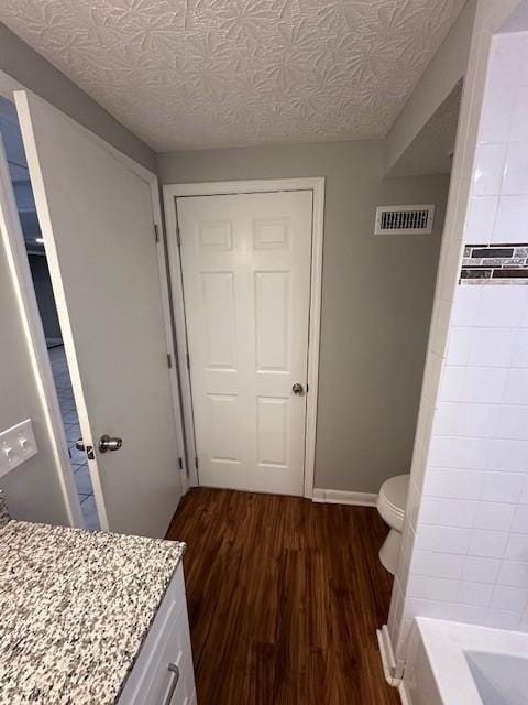 bathroom with a tub to relax in, toilet, a textured ceiling, vanity, and hardwood / wood-style floors