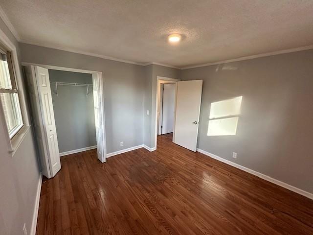 unfurnished bedroom featuring a textured ceiling, baseboards, dark wood-style flooring, and ornamental molding