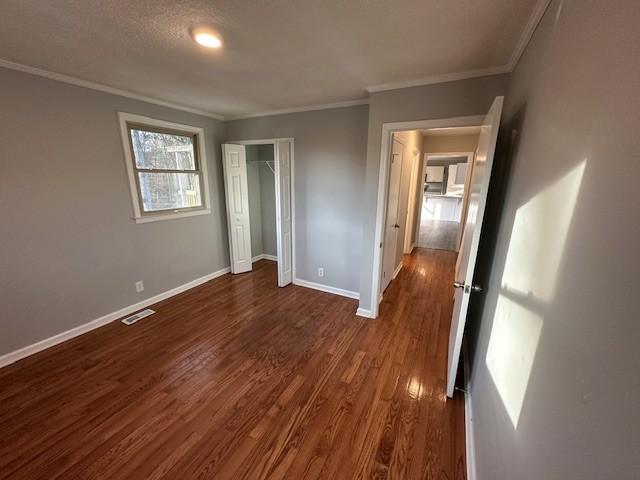 unfurnished bedroom featuring a closet, visible vents, dark wood-type flooring, ornamental molding, and baseboards