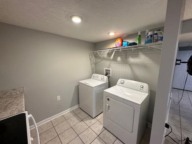 laundry area featuring a textured ceiling, light tile patterned floors, washing machine and dryer, laundry area, and baseboards