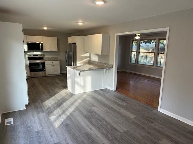 kitchen featuring light stone counters, dark wood-style flooring, stainless steel appliances, white cabinetry, and baseboards