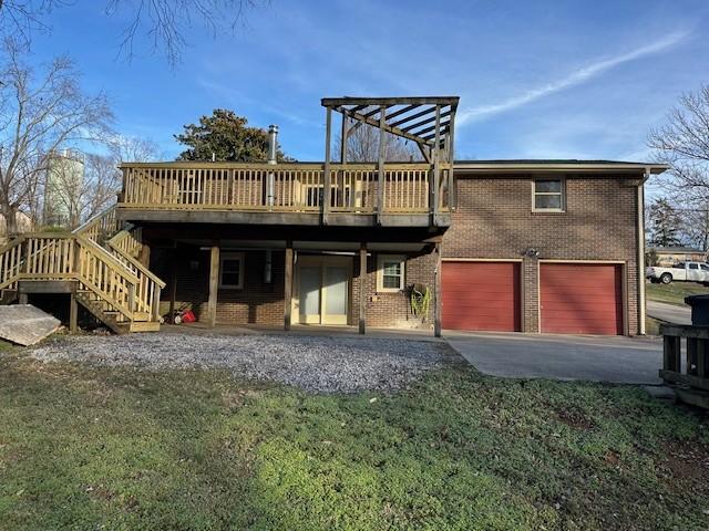 rear view of property with driveway, a garage, a wooden deck, a yard, and brick siding