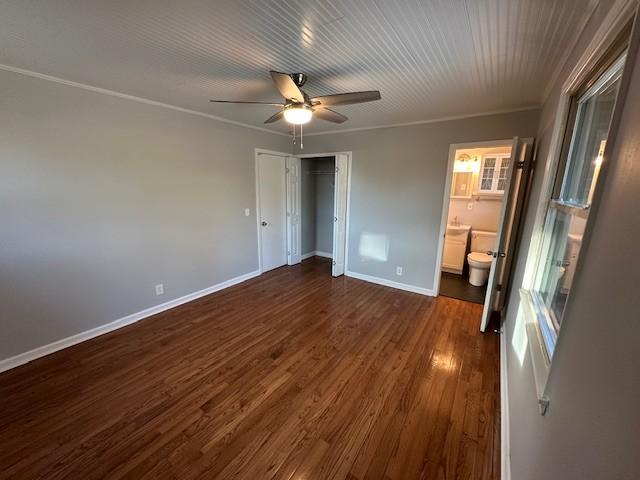 unfurnished bedroom featuring connected bathroom, dark wood-style flooring, a ceiling fan, baseboards, and a closet