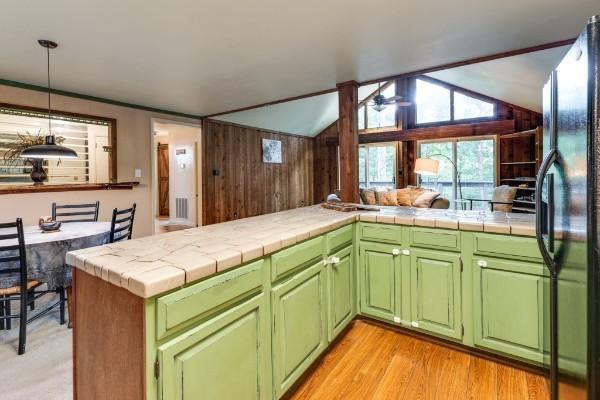 kitchen with lofted ceiling, tile countertops, kitchen peninsula, and black fridge