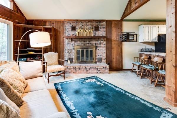 living room featuring vaulted ceiling, a brick fireplace, carpet floors, and wooden walls