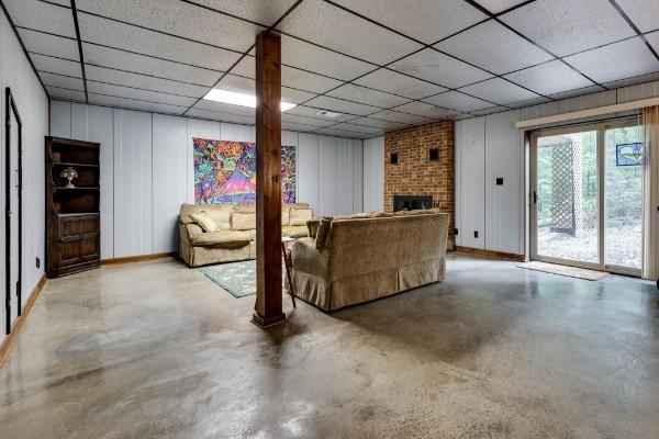 living room featuring a drop ceiling, a brick fireplace, and concrete floors