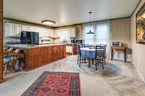 kitchen featuring pendant lighting, white cabinetry, tasteful backsplash, black refrigerator with ice dispenser, and stainless steel dishwasher