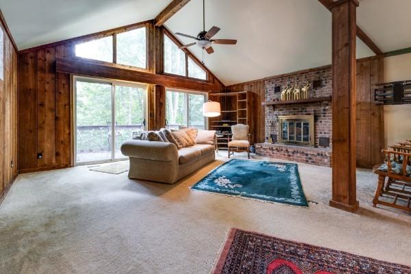 carpeted living room featuring beam ceiling, wooden walls, high vaulted ceiling, decorative columns, and a brick fireplace