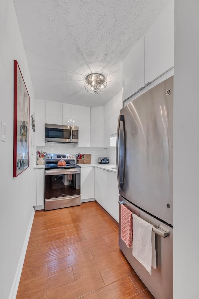 kitchen featuring a textured ceiling, light wood-type flooring, white cabinets, stainless steel appliances, and backsplash