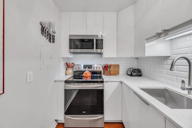 kitchen featuring sink, backsplash, stainless steel appliances, light stone counters, and white cabinets